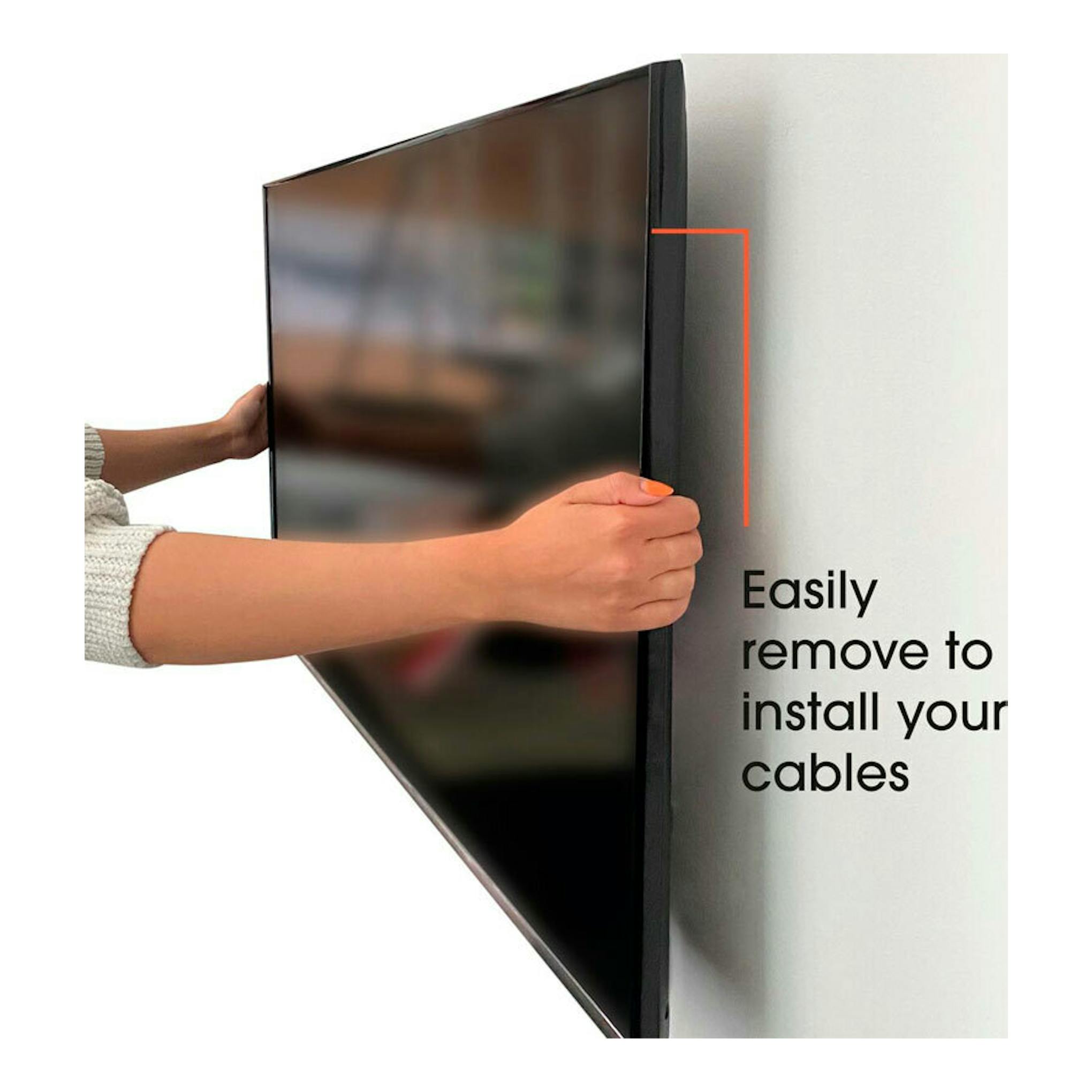 Soporte TV Vogels MA2000: televisor negro montado en pared, sostenido por unas manos para retirar y conectar cables.