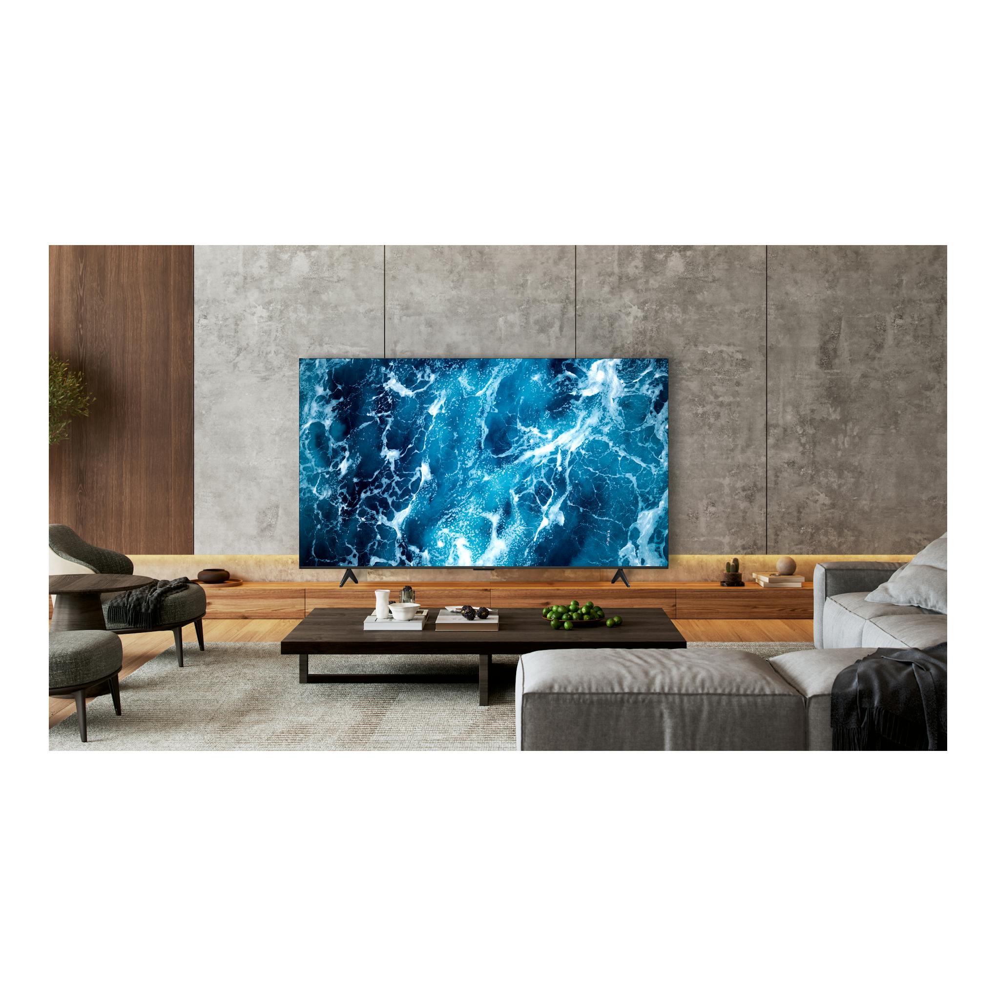 Televisor TCL 55T69C, vista frontal, en un salón moderno, con pantalla mostrando una imagen azul abstracta.