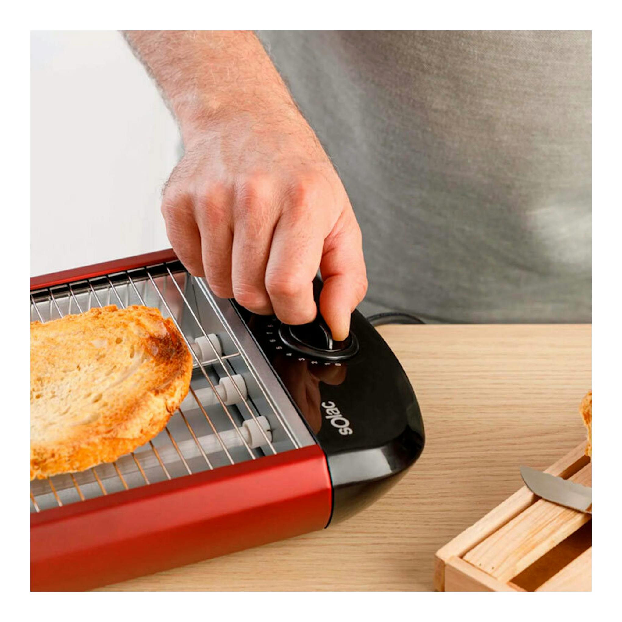 Tostador Solac TC5309 rojo y negro, vista parcial superior, con una rebanada de pan y una mano ajustando el mando.