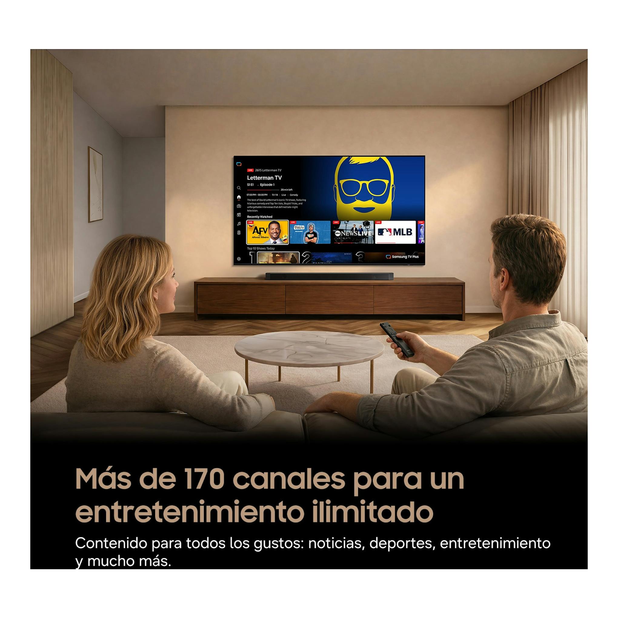 Televisor Samsung TU55M73HAUXXC montado en pared, con interfaz Smart TV y dos personas frente a él.