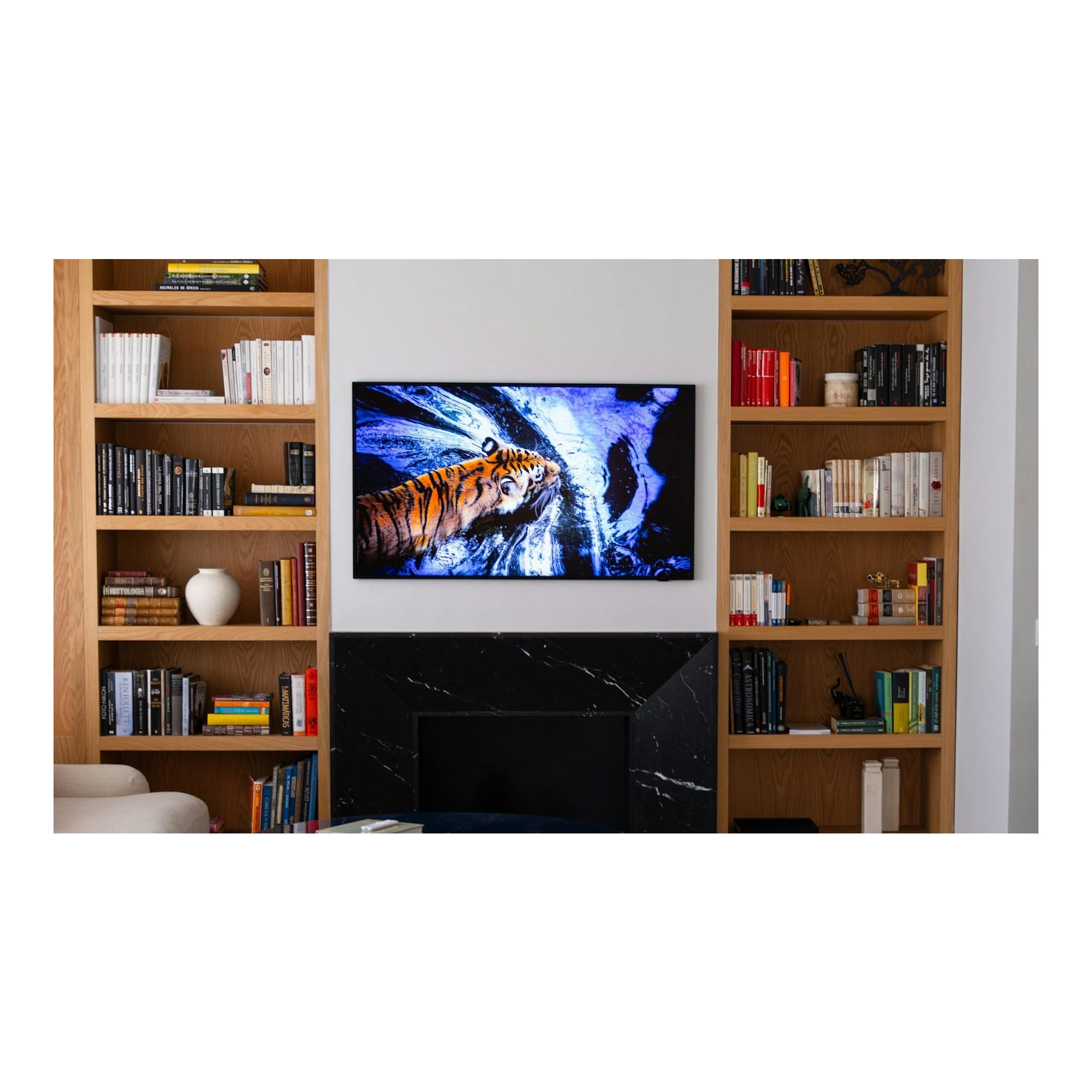 Samsung TQ43LS03HEUXXC: TV negra en vista frontal, montada en pared, con imagen de un tigre; estanterías de madera.