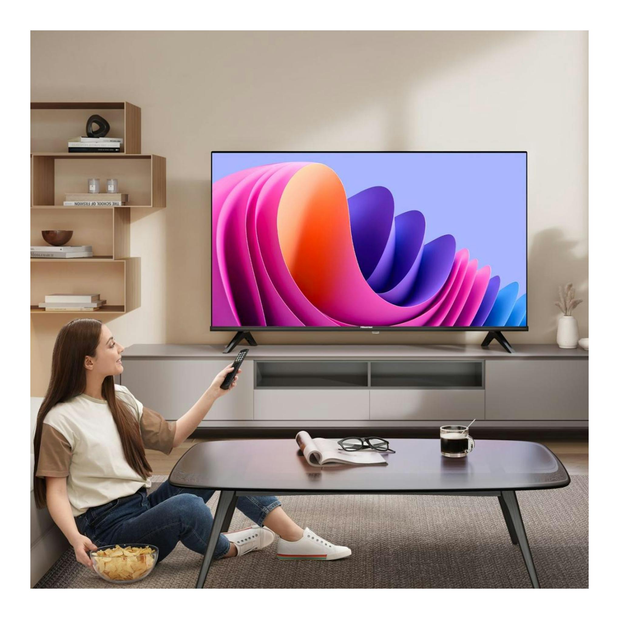Televisor Hisense negro, vista frontal, sobre mueble, con mujer sentada usando un mando a distancia.