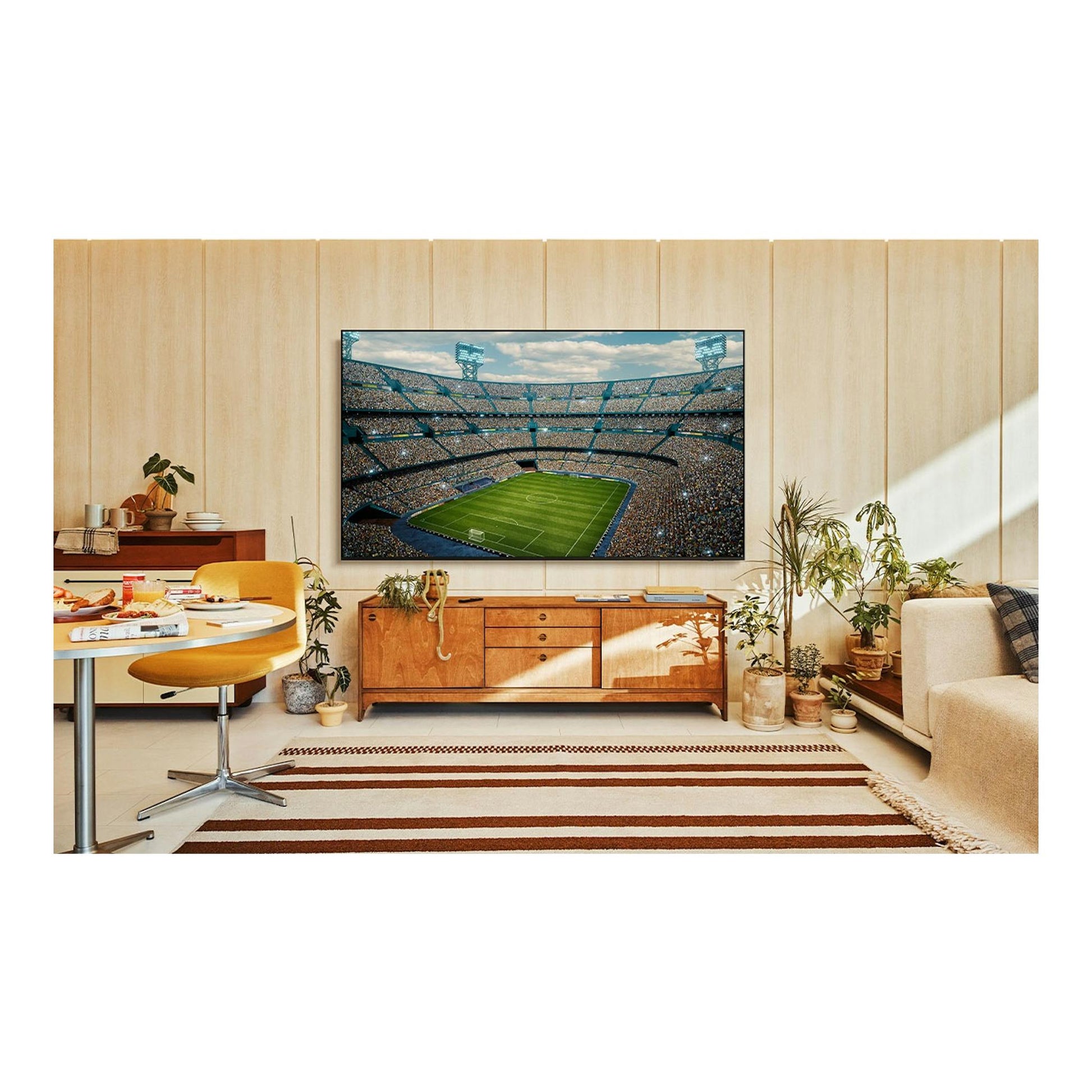 Samsung TU85U7005FKXXC: televisor LED negro montado en pared, con un estadio de fútbol en pantalla, en un salón.