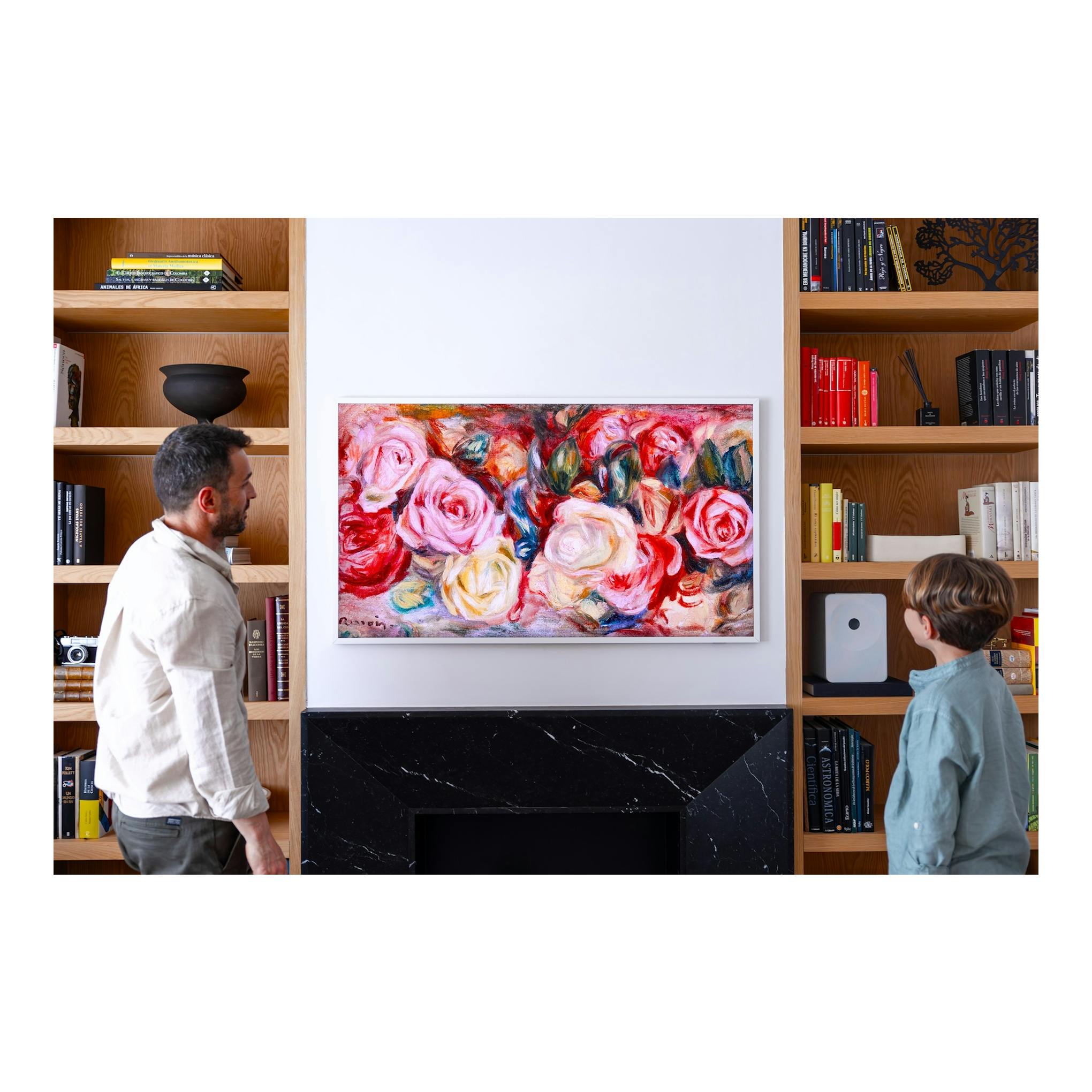 Salón con obra floral enmarcada entre estanterías de madera y dos personas de pie