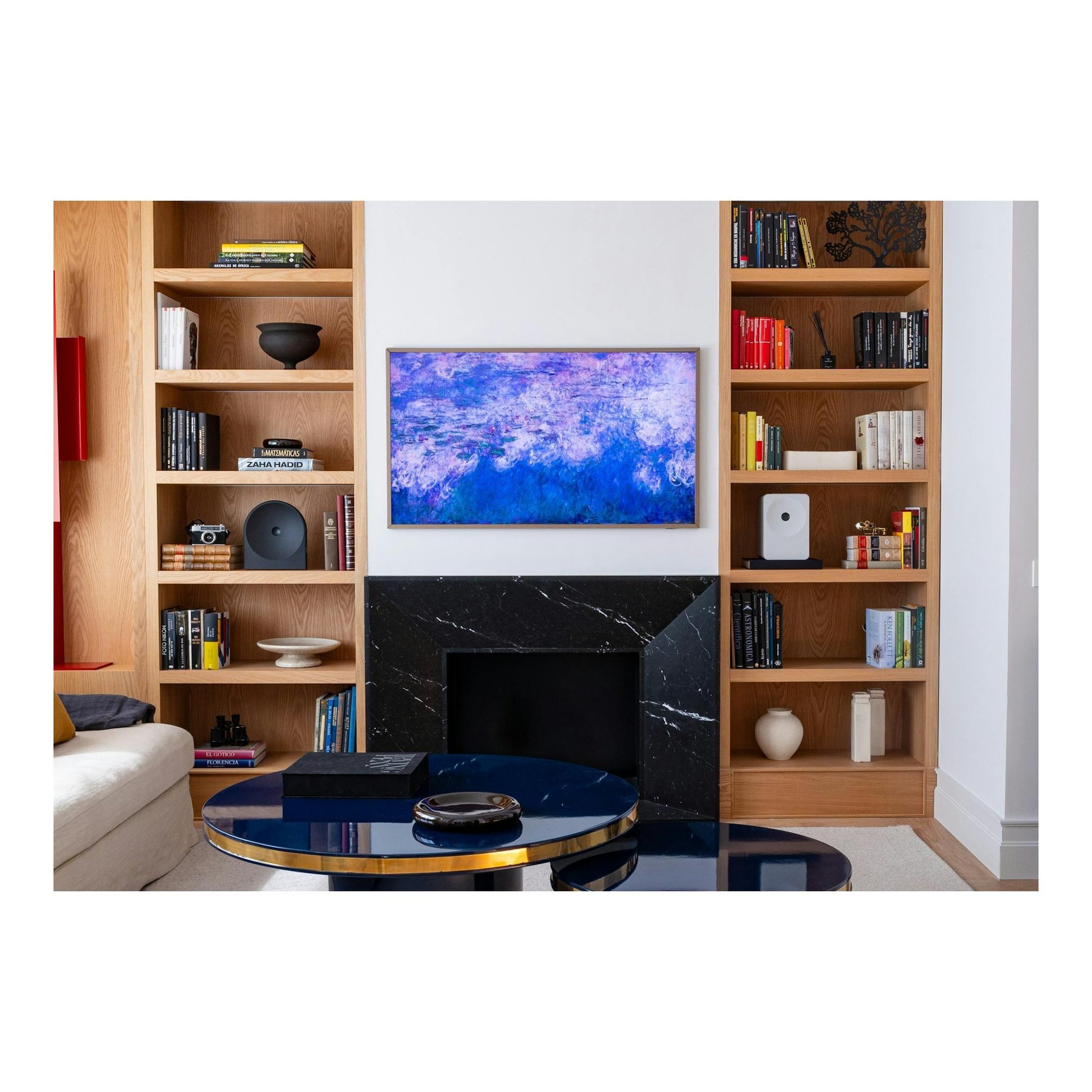 Televisor Samsung The Frame montado en pared blanca, con marco color madera y pantalla con imagen azul.
