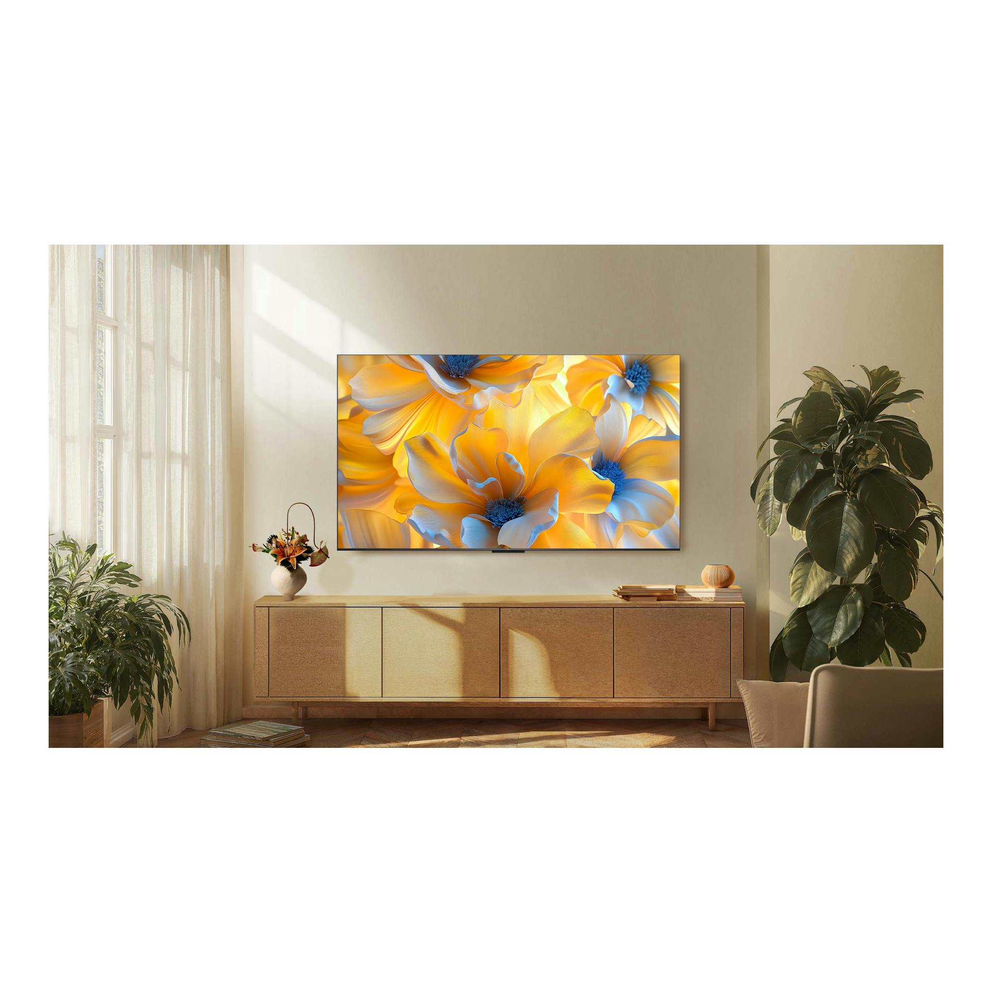 Televisor TCL 65C6K Pro montado en pared, vista frontal, con flores amarillas y azules en pantalla.